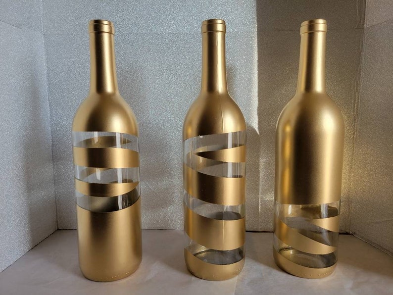 May include: Three gold glass bottles with a clear spiral design. The bottles are empty and have a gold metallic finish.