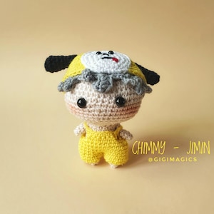 Puede incluir: Muñeca de ganchillo hecha a mano con forma de personaje de dibujos animados. La muñeca tiene un atuendo amarillo, un sombrero amarillo y blanco y ojos negros. El texto "CHIMMY - JIMIN @GIGIMAGICS" es visible.