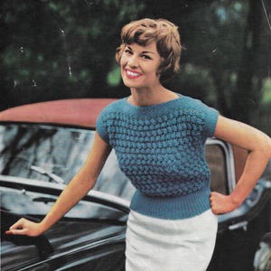 May include: A vintage knitting pattern featuring a woman wearing a blue knitted sweater with a white skirt. The pattern is for a sweater with a 34-36 inch bust and is made with Motoravia Double Knitting Wool. The pattern is mothproofed and costs 7 ounces.