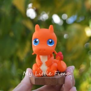 May include: Orange and white figurine of a Pokemon character with blue eyes. The figurine is sitting on a wooden base.