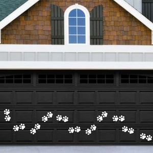 May include: A black garage door with white paw print decals. The garage door has a window with a curved top and a series of horizontal panels.