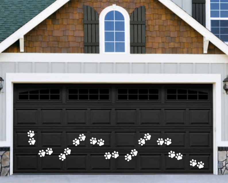 May include: A black garage door with white paw print decals. The garage door has a window with a curved top and a series of horizontal panels.