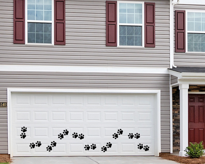 May include: A white garage door with a black number "1140" on the left side. A row of black paw prints are on the bottom of the door.