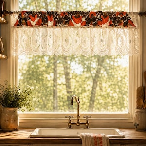 May include: A window valance featuring a top band of dark brown fabric with a vibrant orange floral pattern, finished with a wide, intricate cream-coloured lace trim that hangs in a scalloped edge across the top of the window frame.