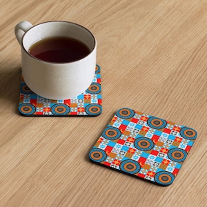 Könnte beinhalten: Eine weiße Tasse mit Tee steht auf einem quadratischen Untersetzer. Der Untersetzer hat ein farbenfrohes geometrisches Muster mit blauen, roten, orangefarbenen und weißen Quadraten und Kreisen. Ein weiterer Untersetzer ist daneben.
