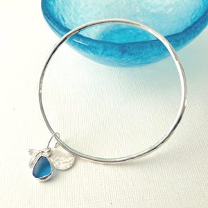 Blue seaglass and silver charm’s on a handmade hammered solid silver bangle.Cornish seaglass and silver charm dangling on full silver bangle