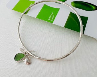 Handmade silver bangle with handmade silver sea shells and silver set deep green sea glass dangling . Handcrafted sterling silver bangle