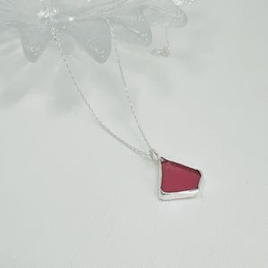 Seaham red/ deep pink sea glass shaped by the waves of the famous sea glass beach in County Durham UK. Set into an open bezel of silver.