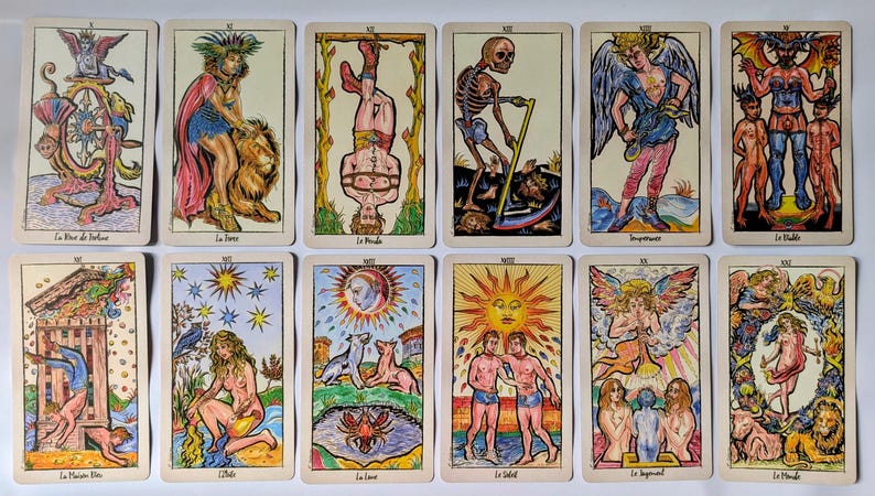 May include: A set of twelve tarot cards arranged in two rows, featuring colorful illustrations of figures and symbols including a skeleton with a scythe, a sun, a devil, and a winged angel, with French text labels at the bottom of each card.