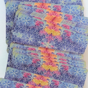 May include: A deck of rectangular cards arranged in a fanned stack. Each card features a repeating geometric pattern of intersecting white circles over a watercolor-style background of blended blue, purple, pink, and yellow hues.