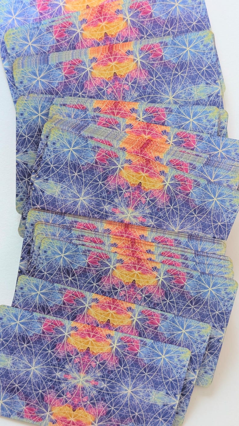 May include: A deck of rectangular cards arranged in a fanned stack. Each card features a repeating geometric pattern of intersecting white circles over a watercolor-style background of blended blue, purple, pink, and yellow hues.