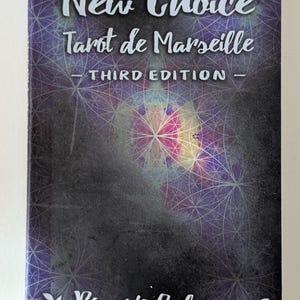 May include: A rectangular book titled New Choice Tarot de Marseille Third Edition by Rosario Salerno. The cover features a dark purple and black background with a white geometric pattern of intersecting circles and a central light burst.