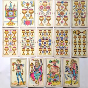 May include: A collection of fourteen tarot cards from the suit of cups, arranged in three rows. The cards feature illustrations of golden chalices, floral motifs, and four human figures, including a page, queen, king, and knight on horseback.