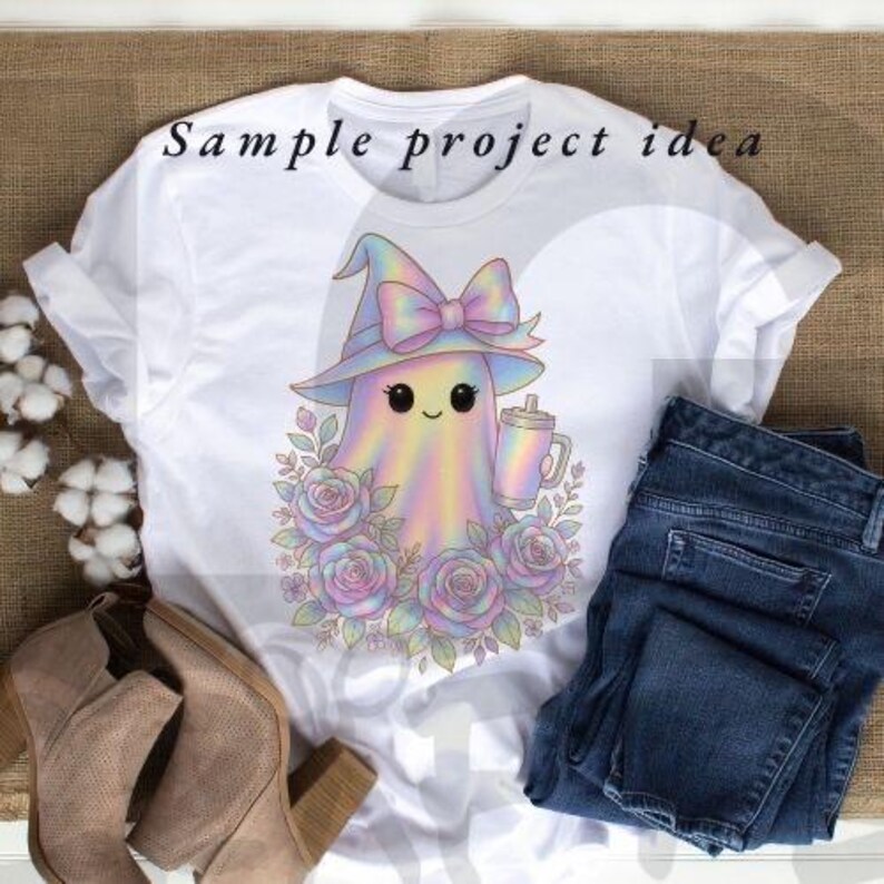 May include: White t-shirt featuring a pastel ghost wearing a witch hat with a bow, holding a drink, and surrounded by roses. The text "Sample project idea" is printed at the top. Paired with blue jeans and tan boots.