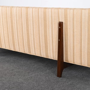 May include: A beige striped sofa with dark brown wooden legs. The sofa is viewed from the back.