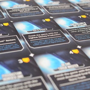 May include: A collection of rectangular game cards with dark blue and black space-themed backgrounds. Each card features a yellow shield icon with a number, white text headers like Gold Digger, and descriptive game instructions in white font.