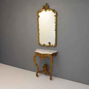 Peut inclure: Un miroir dor&eacute; avec des d&eacute;tails orn&eacute;s au-dessus d'une console peinte en or avec un plateau en marbre blanc.