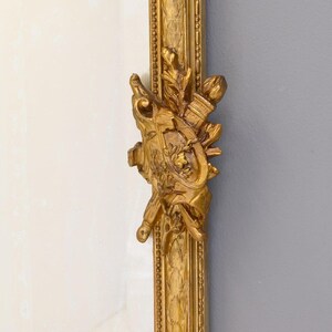 May include: A gold-colored ornate frame with intricate carvings and a decorative design. The frame is made of wood and has a smooth, polished finish.