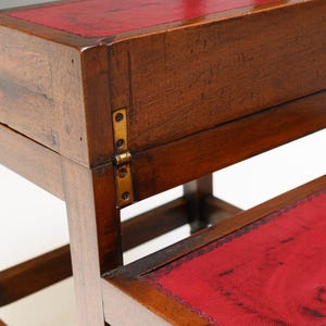 Puede incluir: Taburete de madera con dos escalones y tapa con bisagras. Los escalones est&aacute;n cubiertos de cuero rojo. La madera tiene un acabado marr&oacute;n oscuro. El taburete tiene bisagras de lat&oacute;n y patas torneadas. Mide unos 60 cm de alto.