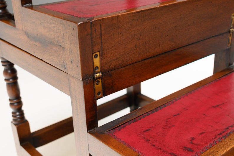 Puede incluir: Taburete de madera con dos escalones y tapa con bisagras. Los escalones est&aacute;n cubiertos de cuero rojo. La madera tiene un acabado marr&oacute;n oscuro. El taburete tiene bisagras de lat&oacute;n y patas torneadas. Mide unos 60 cm de alto.