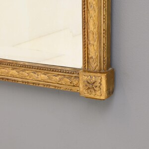 May include: A gold-colored ornate mirror frame with intricate carvings. The frame is made of wood and has a beveled edge.