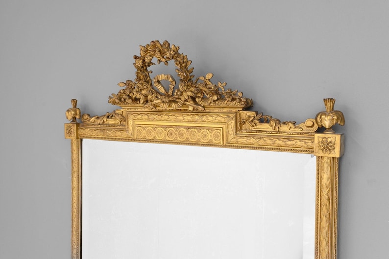 May include: A gold-toned ornate mirror with a decorative floral design at the top and a rectangular frame.