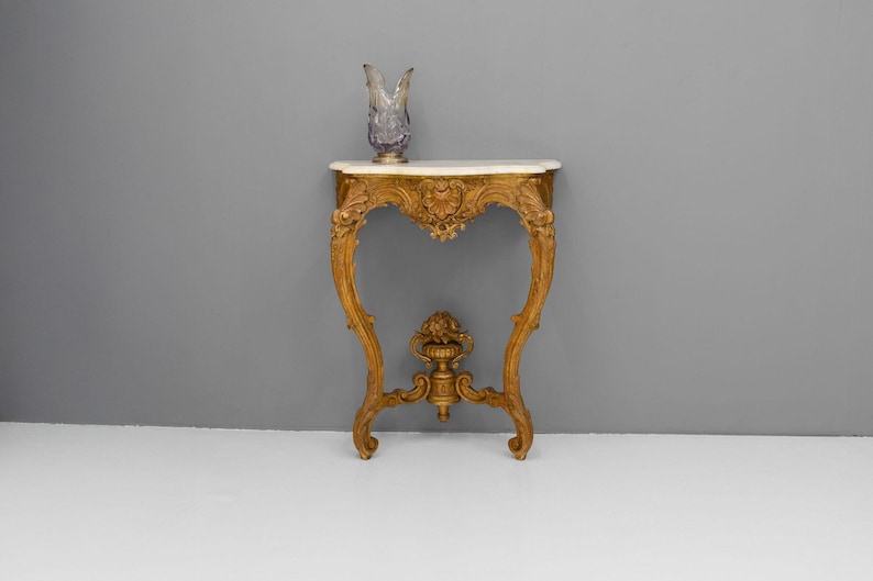 Peut inclure: Une console en bois peinte en or avec un plateau en marbre blanc. La table a un design sculpt&eacute; et un style d&eacute;licat et orn&eacute;.