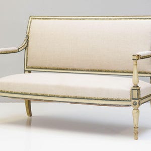 May include: A white and gold painted wooden settee with a light beige fabric cushion. The settee has a curved back and a simple design.