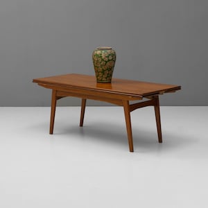 May include: A mid-century modern extendable table with a wood top and legs. The table is made of solid wood and has a natural finish. A green and brown ceramic vase sits on the table.