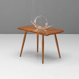 May include: A mid-century modern side table with a clear glass sculpture. The table has a rectangular top and four angled wooden legs. The glass sculpture is an abstract design with curved lines.