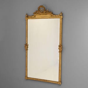 May include: A large, ornate gold mirror with a decorative frame. The frame is carved with intricate details and has a central crest at the top.