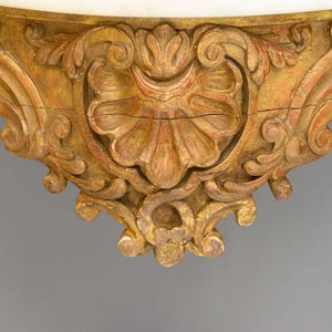 Peut inclure: Gros plan sur la base d'une console en bois orn&eacute;e, peinte en or, avec des sculptures complexes. La base pr&eacute;sente un motif central en forme de coquille avec des motifs floraux tourbillonnants.