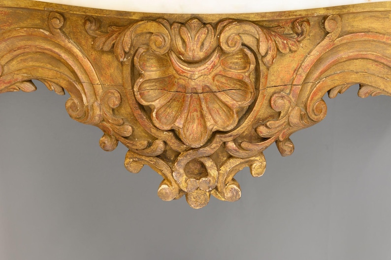 Peut inclure: Gros plan sur la base d'une console en bois orn&eacute;e, peinte en or, avec des sculptures complexes. La base pr&eacute;sente un motif central en forme de coquille avec des motifs floraux tourbillonnants.