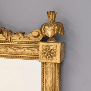 May include: A gold-toned ornate mirror frame with intricate carvings and a decorative top. The frame is made of wood and has a distressed finish.