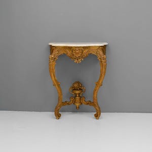 Peut inclure: Une console en bois peinte en or avec un plateau en marbre blanc et des sculptures complexes. La table a un design incurv&eacute; et ouvert et repose sur trois pieds.