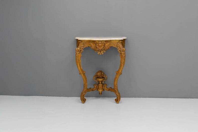 Peut inclure: Une console en bois peinte en or avec un plateau en marbre blanc et des sculptures complexes. La table a un design incurv&eacute; et ouvert et repose sur trois pieds.