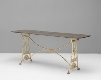 May include: A vintage cast iron table with a distressed white finish and a rectangular top. The table has a simple, elegant design with curved legs and a crossbar.
