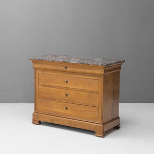 Puede incluir: Cómoda de madera con tres cajones y tapa de mármol. La cómoda es de madera de color marrón claro y tiene forma rectangular. La tapa de mármol tiene un diseño gris y blanco.