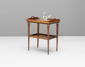 May include: A two-tiered wooden serving table with a brown finish and gold accents. The table has a rectangular top and a lower shelf. A crystal serving bowl sits on the top shelf.