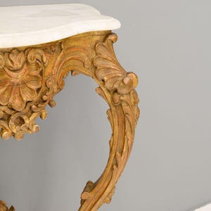 Peut inclure: Une console en bois peinte en or avec un dessus en marbre blanc et des sculptures complexes. La table a une jambe incurv&eacute;e et orn&eacute;e.