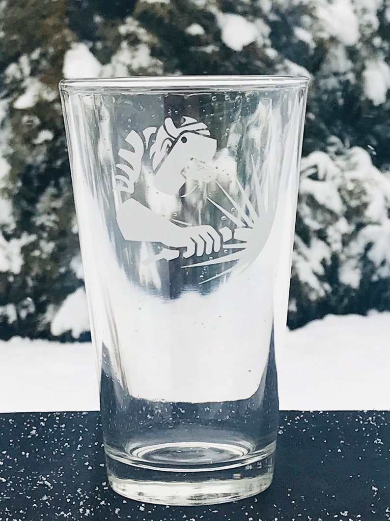 May include: A clear glass pint glass with an etched design of a welder wearing a welding mask and holding a welding torch.