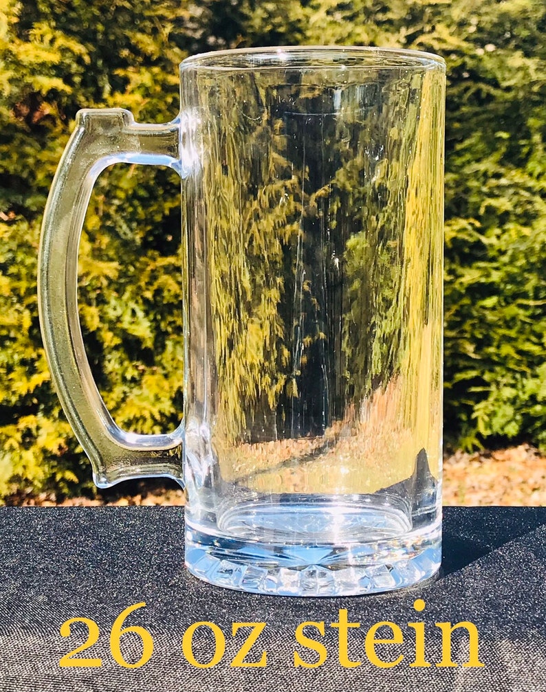 May include: A clear glass 26 ounce stein with a handle. The stein is sitting on a black surface.