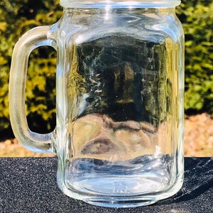 May include: A clear glass pint mug with a handle. The mug is empty and sitting on a black surface.