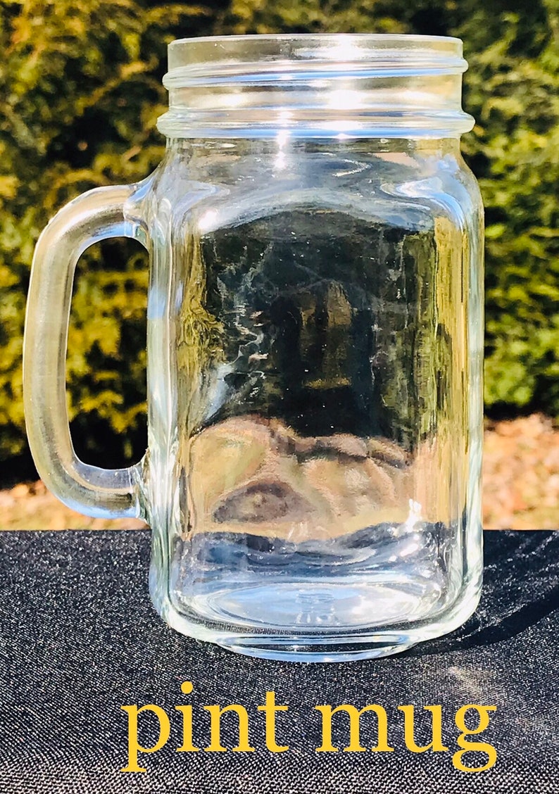 May include: A clear glass pint mug with a handle. The mug is empty and sitting on a black surface.
