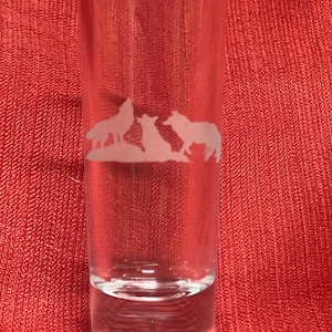 May include: A clear glass shot glass with an etched design of three wolves. The wolves are facing the left side of the glass.
