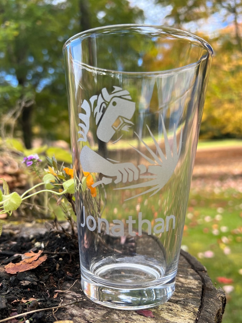 May include: A clear glass beer stein with a white etched design of a person welding. The name "Jonathan" is etched below the design.