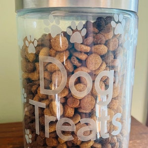 May include: A clear glass jar with a silver lid filled with dog treats. The jar has a paw print design and the words "Dog Treats" etched into the glass.