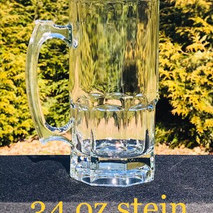 May include: A clear glass 34 oz stein with a handle. The stein has a textured design and is sitting on a black surface.