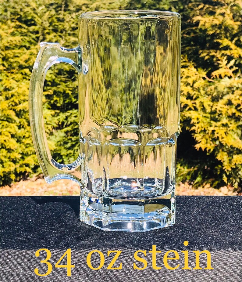 May include: A clear glass 34 oz stein with a handle. The stein has a textured design and is sitting on a black surface.