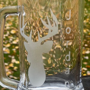 Könnte beinhalten: Ein klares Glasbierkrug mit einem mattierten Design eines Hirschkopfes und Geweihs. Der Name "Jordan" ist auf die Seite des Kruges geätzt.